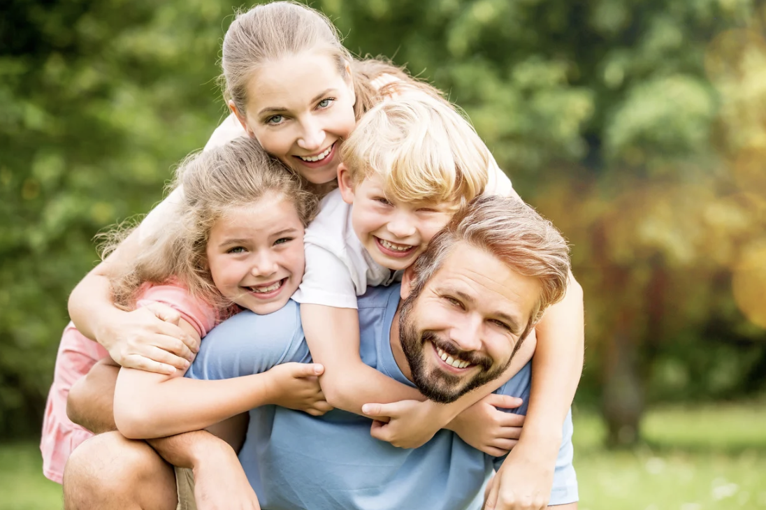 Parents heureux Une famille souriante avec deux enfants, jouant dans un parc verdoyant.
